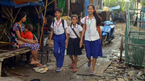 Children in school uniforms walk through the impoverished neighborhood in which they live