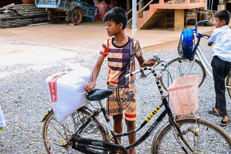Un petit garçon remonte sur son vélo avec son sac de riz après une distribution à Oudong
