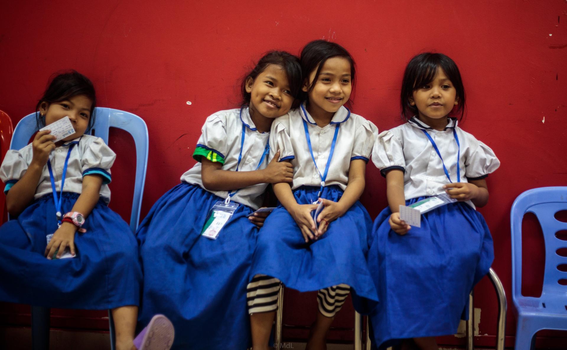 Un groupe de fillettes en uniforme scolaire assises sur des chaises devant un mur rouge