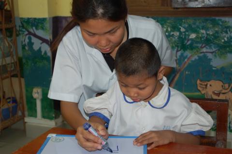 Une éducatrice spécialisée aide un enfant porteur de handicap à écrire